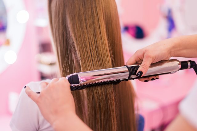 young woman getting her hair curled by stylist at parlor. Beautiful young hairdresser giving new haircut to female in saloon